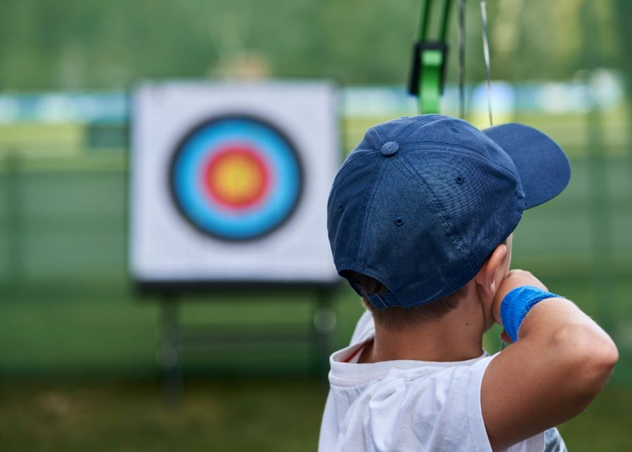Bambino con cappellino che tira con l'arco verso un bersaglio